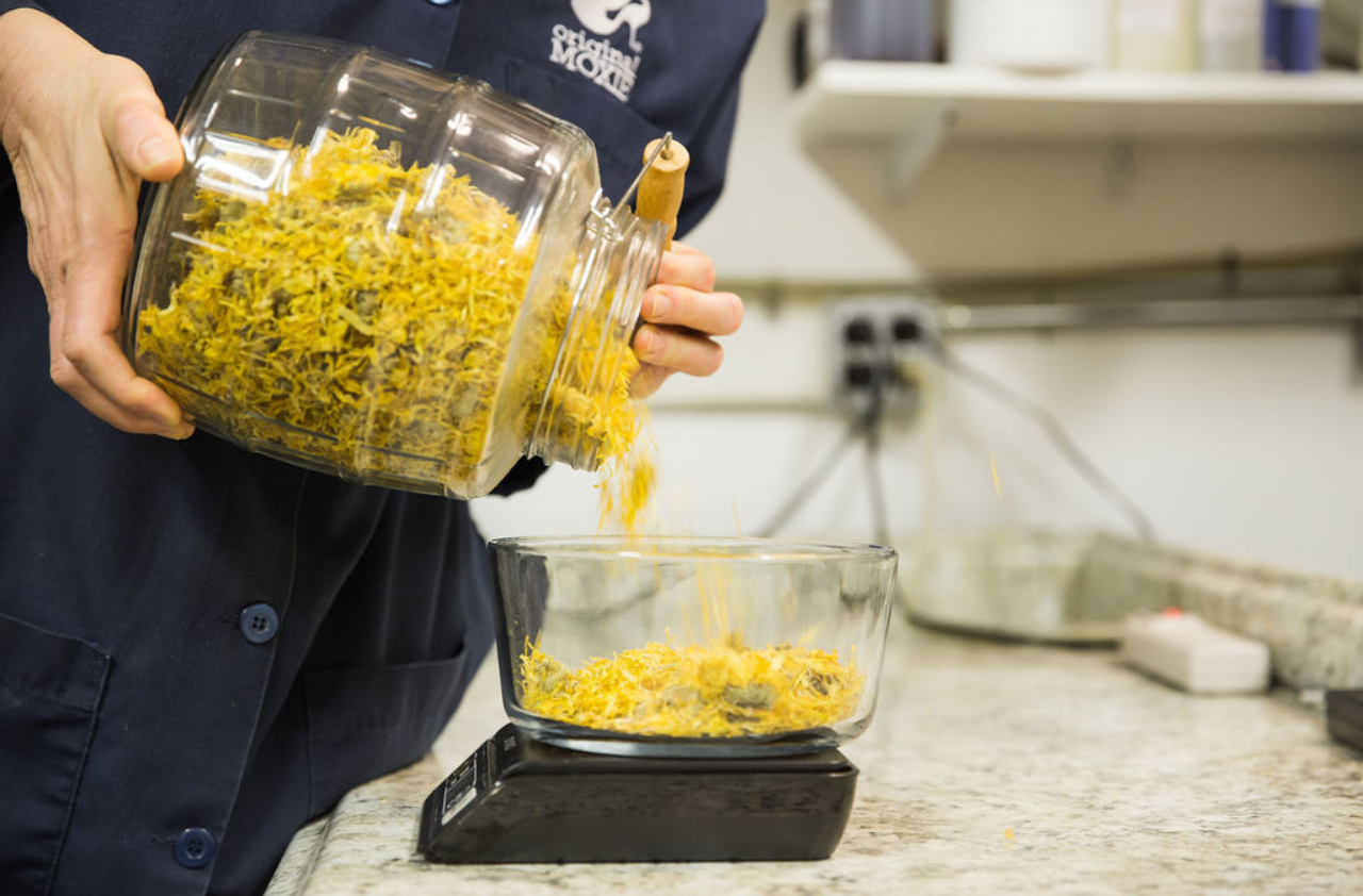 Product-formulator pouring dried herbs into a bowl on a scale