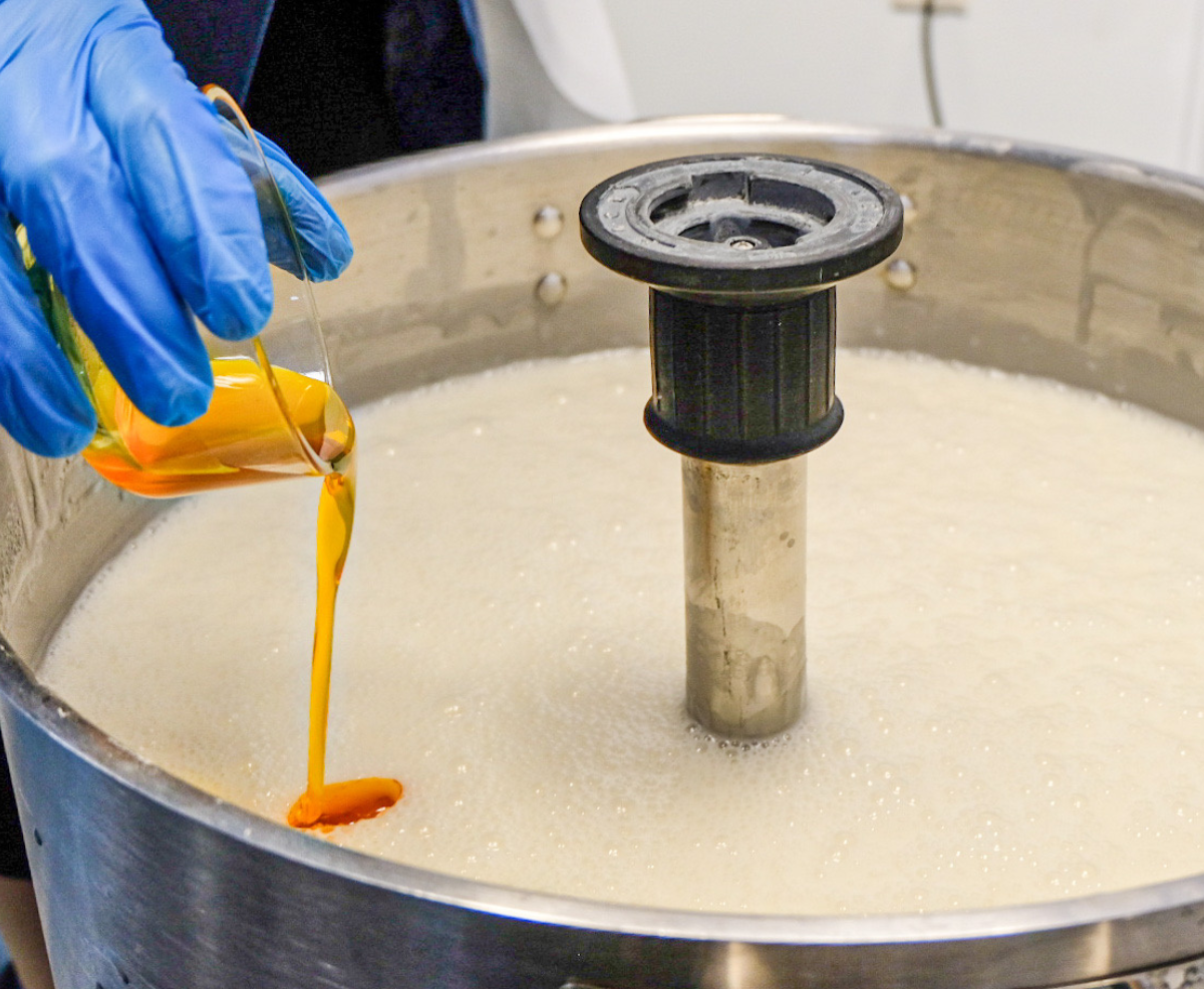 A product-formulator pouring an ingredient into a mixing vessel 