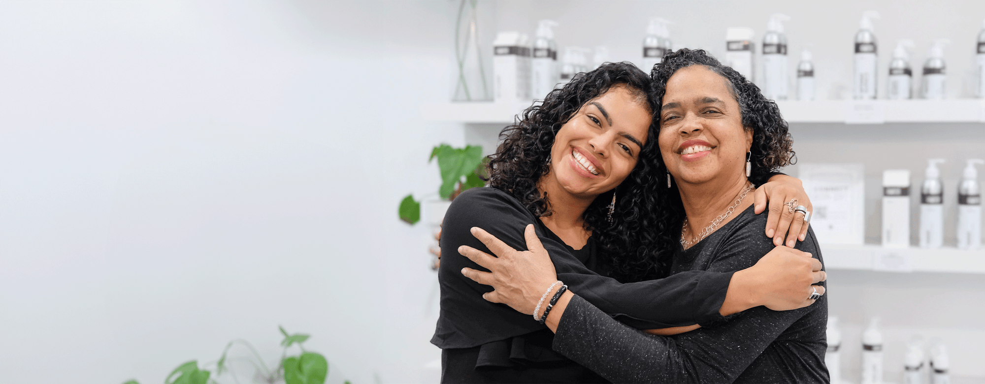 Two women with curly hair hugging and smiling