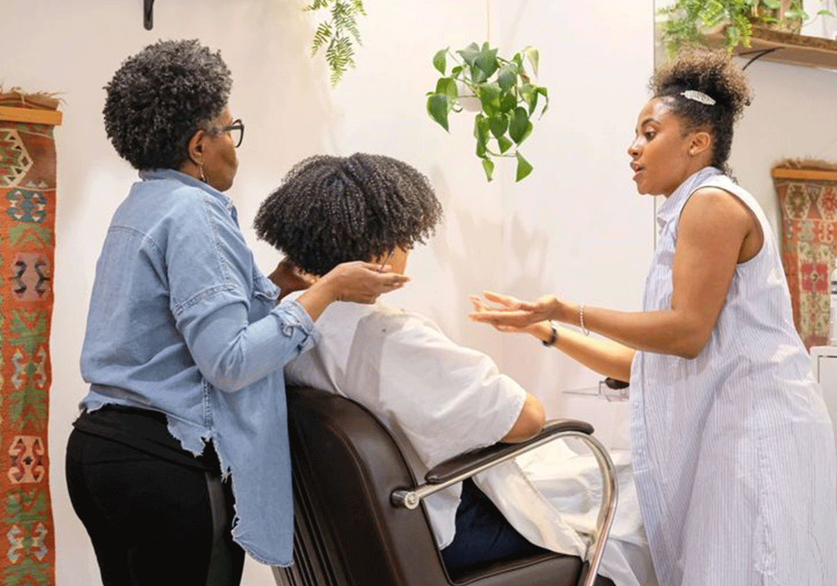 A hair stylist helping another stylist with a curly haircut 